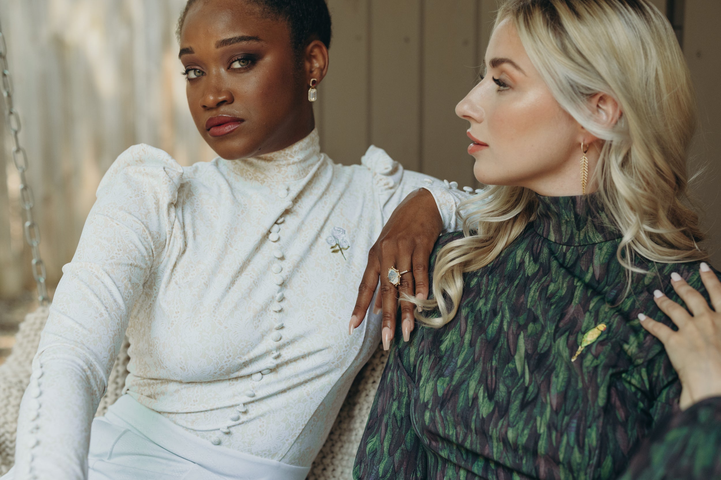 Two women wearing the I Do and Going Somewhere jumpsuits, showcase sparkling jewelry from Kelly Wade Jewelers with Mrs Momma Bear outfits in a natural outdoor setting.