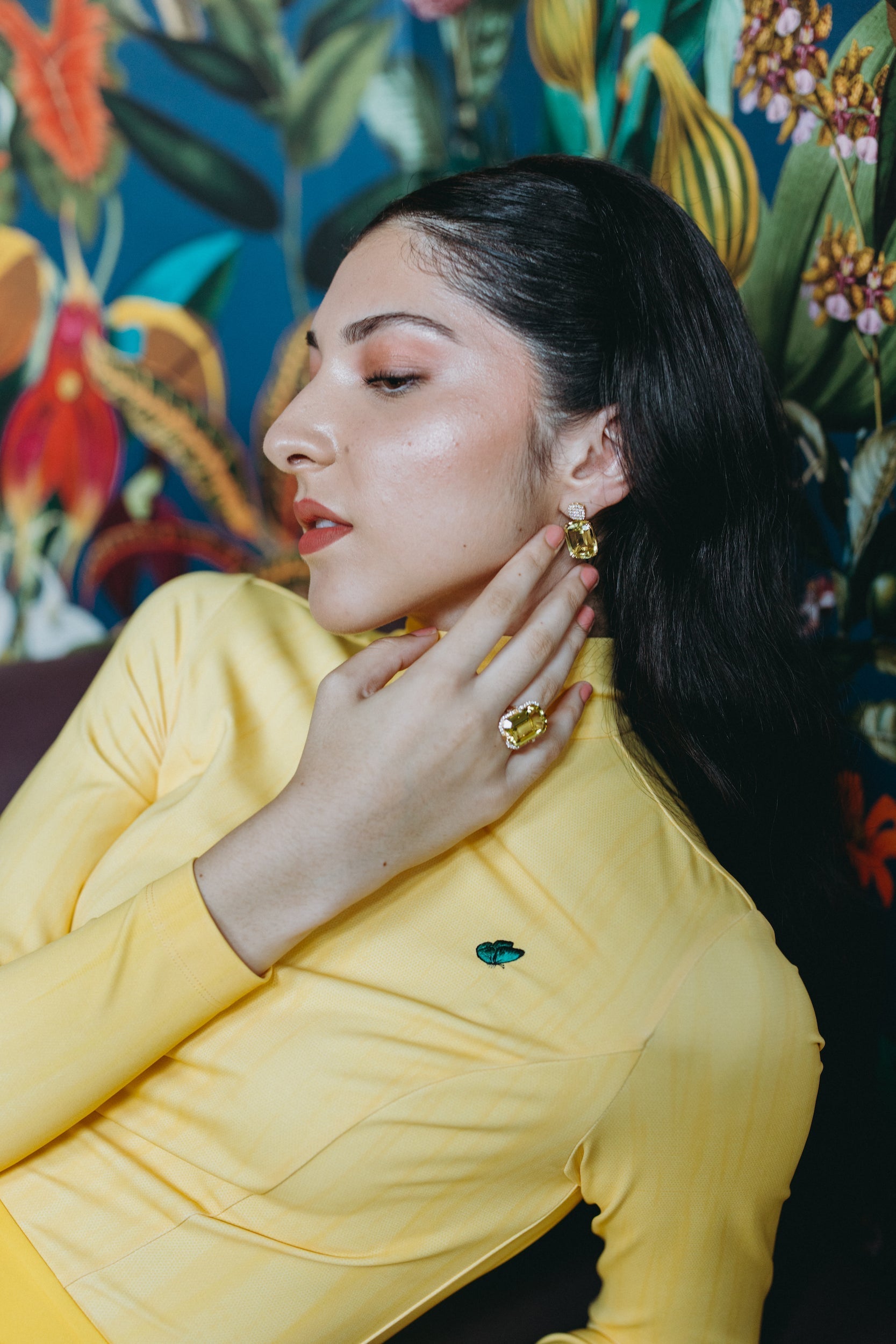 Model showcasing Goshwara jewelry while wearing the yellow Milano jumpsuit against a vibrant floral background.