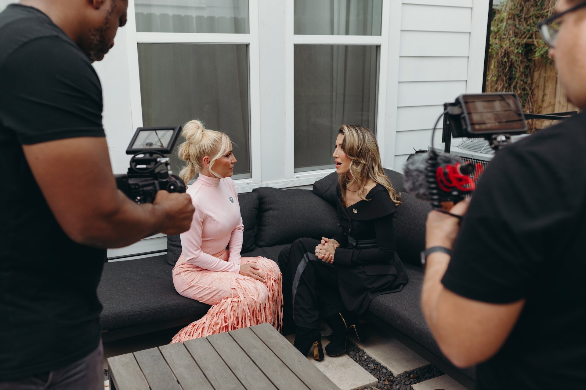 Lee Evans Lee engage in a discussion with breast cancer survivor on a couch while being filmed by a crew, promoting breast cancer awareness, wearing Dancing Anyone 