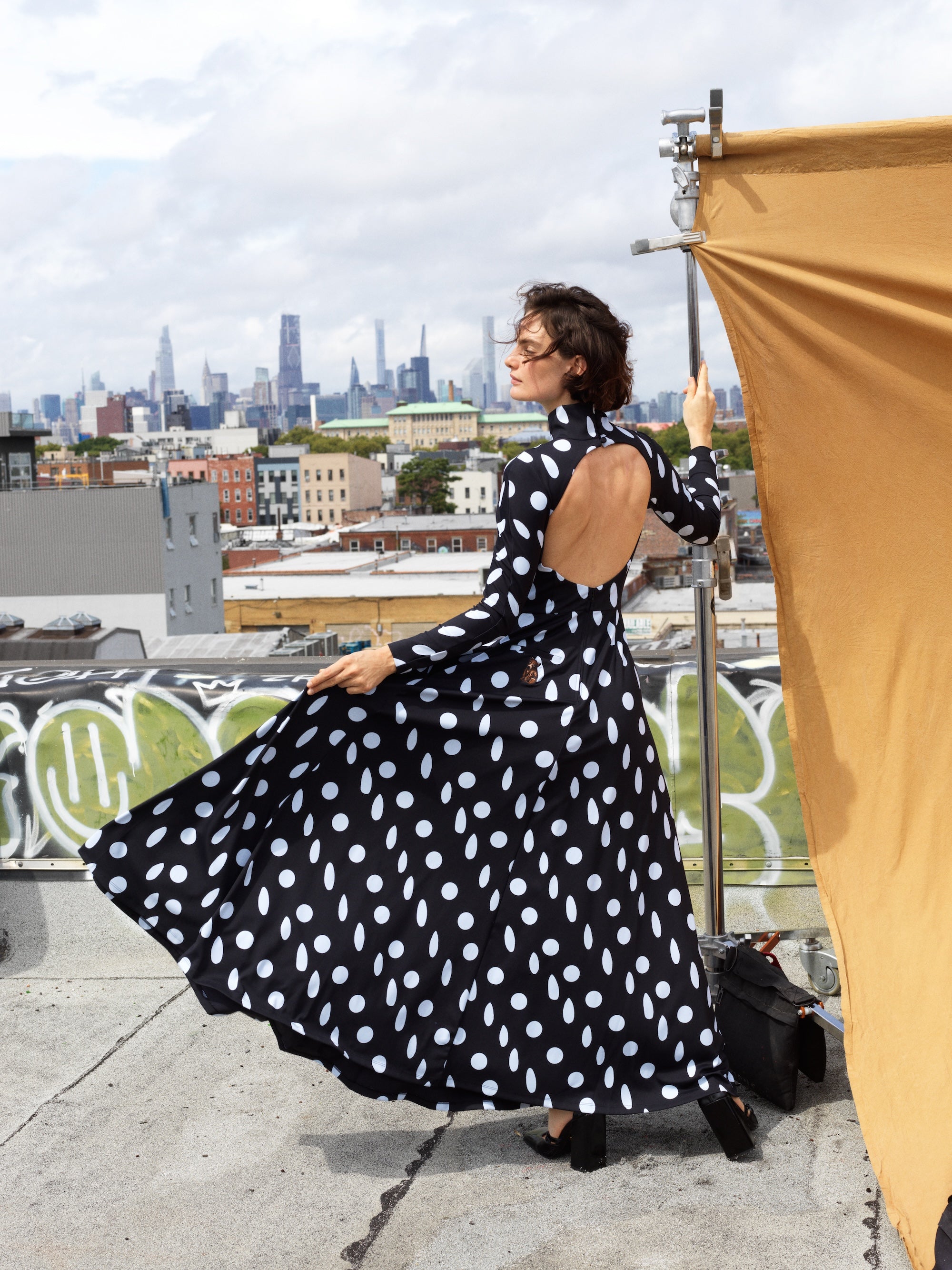 Woman in Sexy Day poses on a rooftop with a city skyline backdrop, showcasing a stylish look.