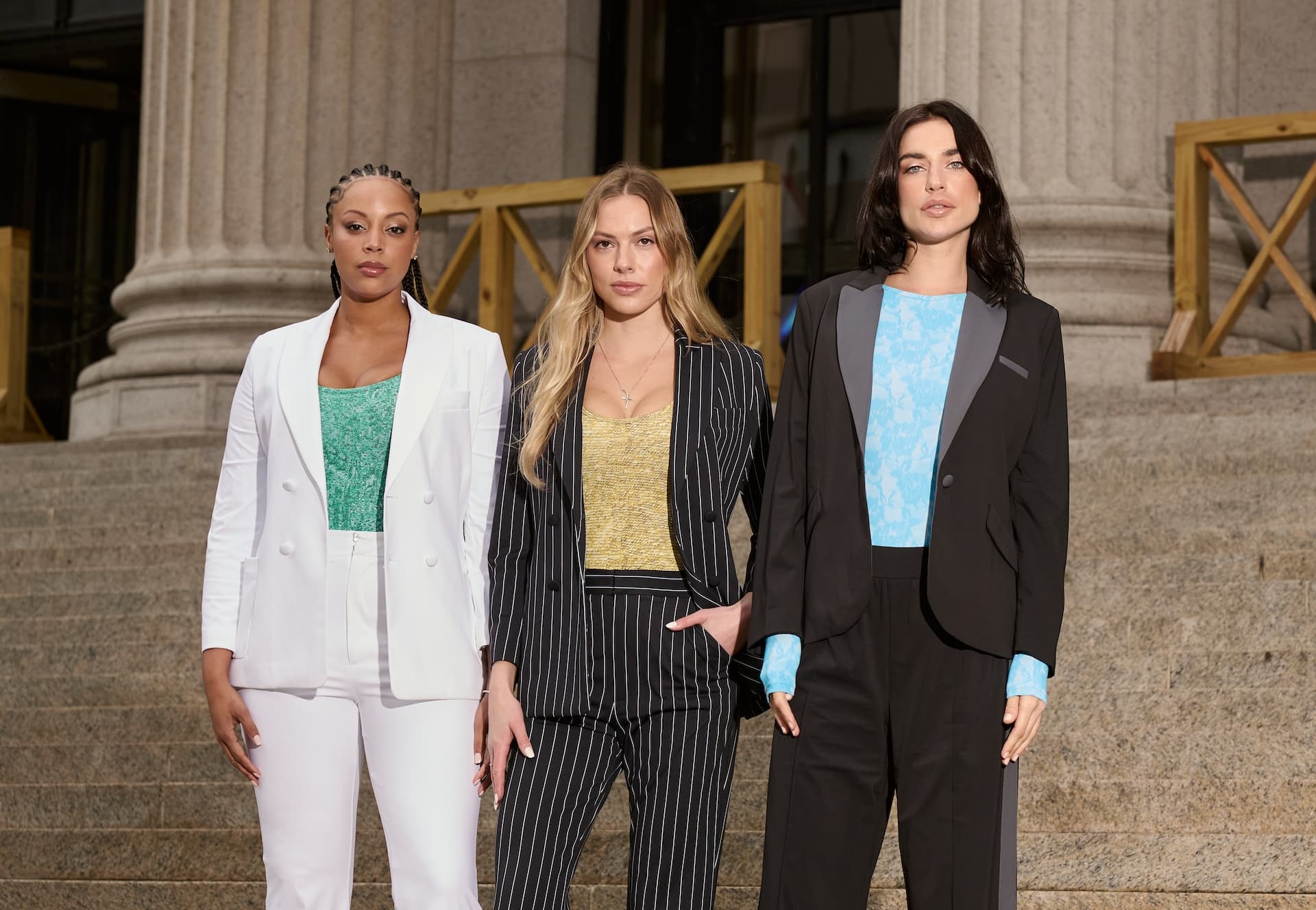 Three models showcase Signature Luxe Tee - Super Star, Signature Luxe Tee - Lucky Lady, and Luxe Long Sleeve Bodysuit - Fellini on outdoor steps, featuring vibrant tops and fashionable outerwear.