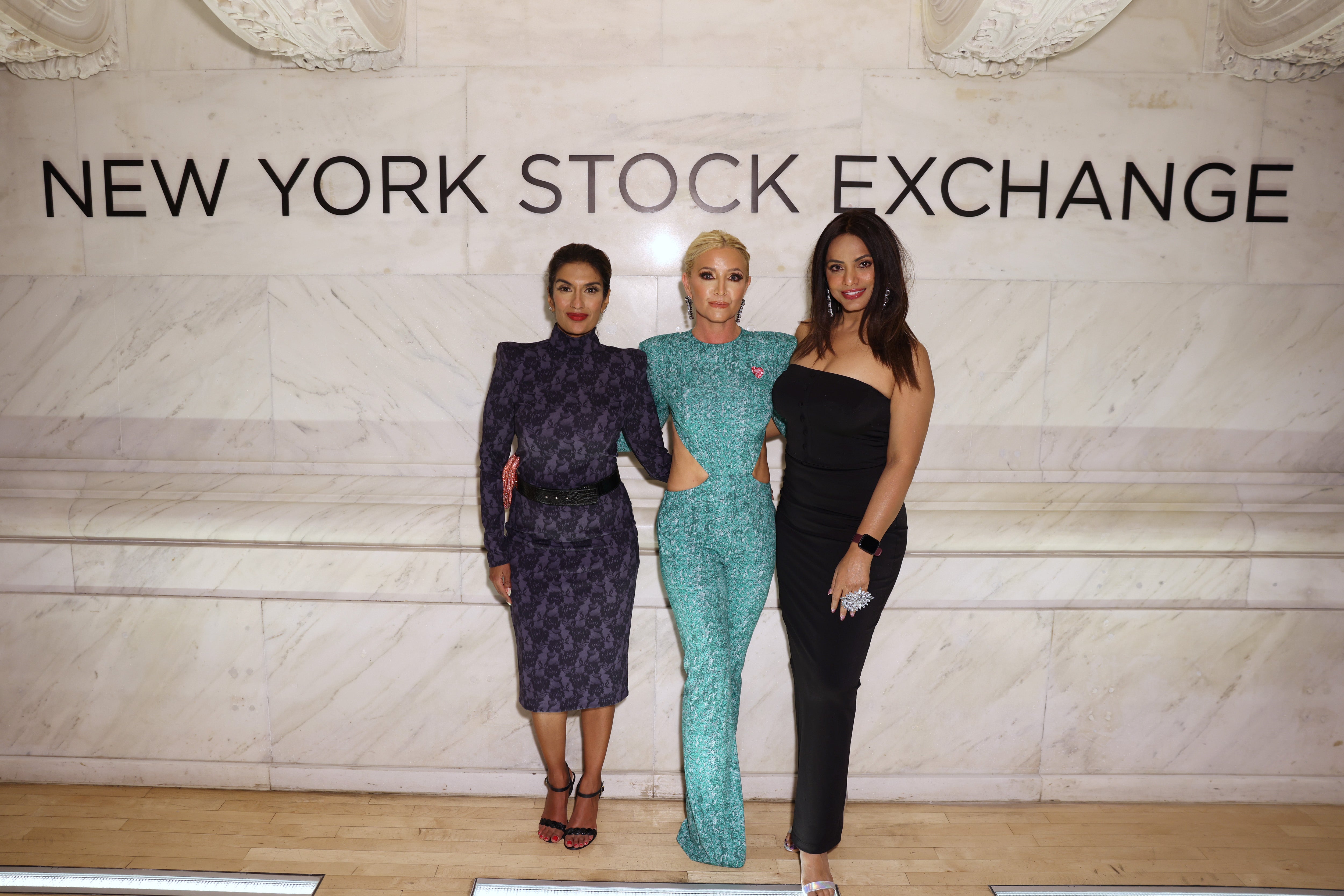 Three women posing elegantly at the New York Stock Exchange, showcasing Black Widow, Fellini, and Look at Me Jumpsuit