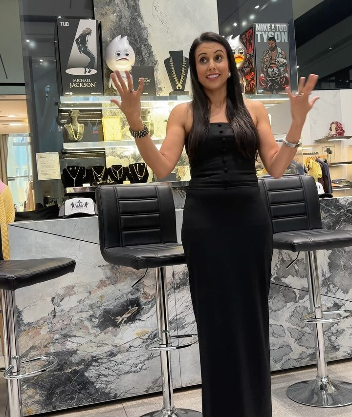 Woman in a black dress gesturing while speaking in a stylish jewelry store with modern decor.