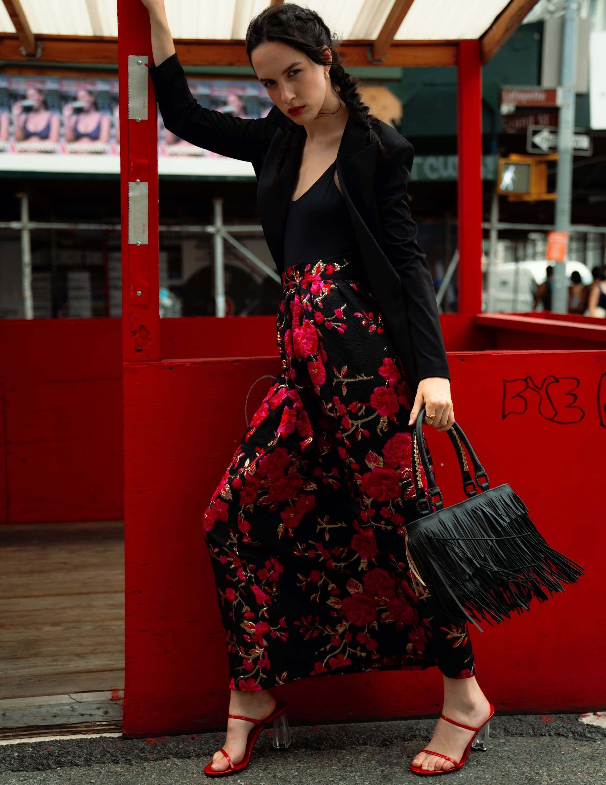 Model in floral maxi skirt Starry Night blazer poses with fringe handbag in urban setting, showcasing trendy fashion style.