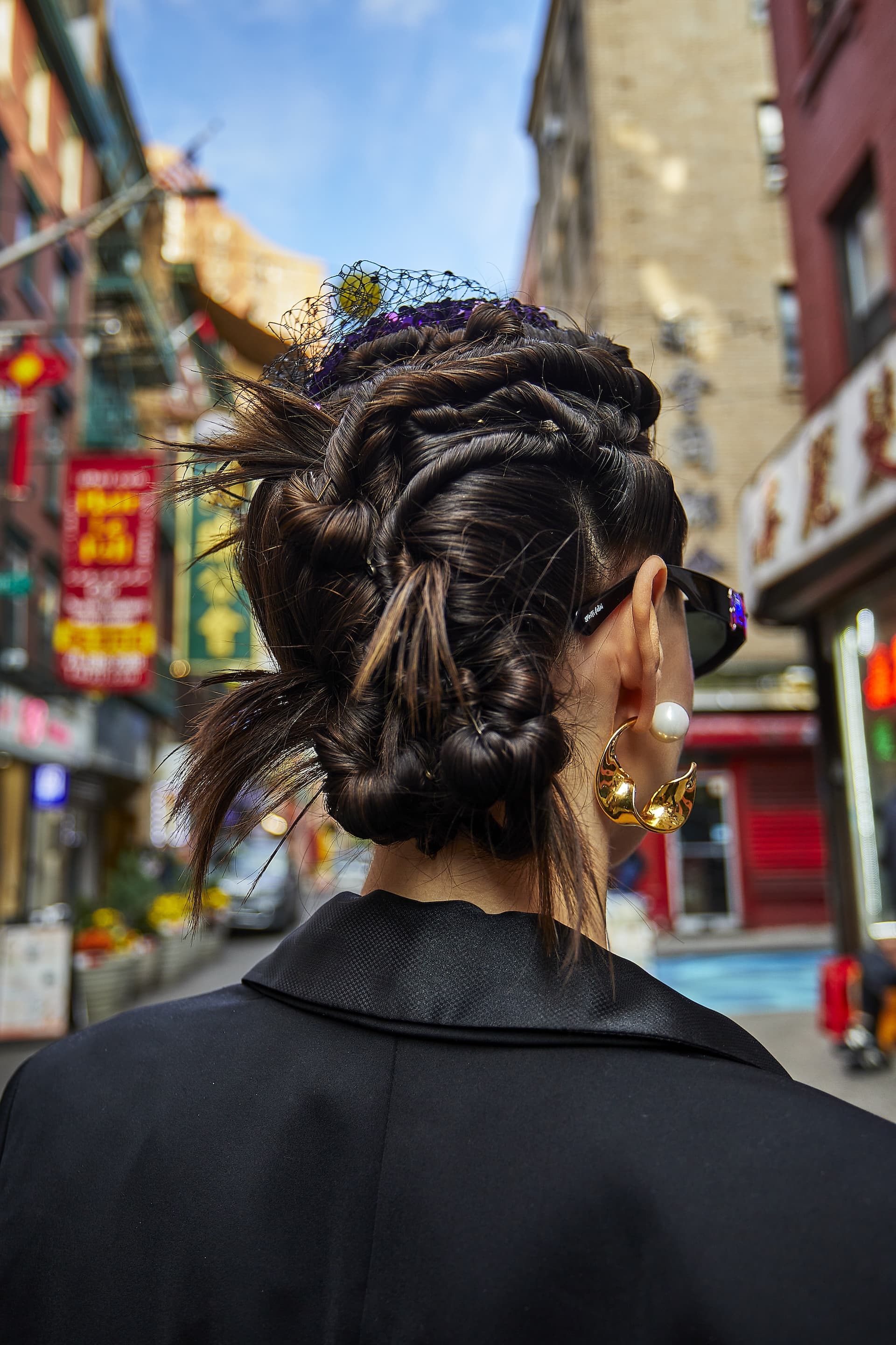 Stylish woman wearing the Starry Night Blazer with intricate braided hairstyle and large earrings walking through a vibrant city street.