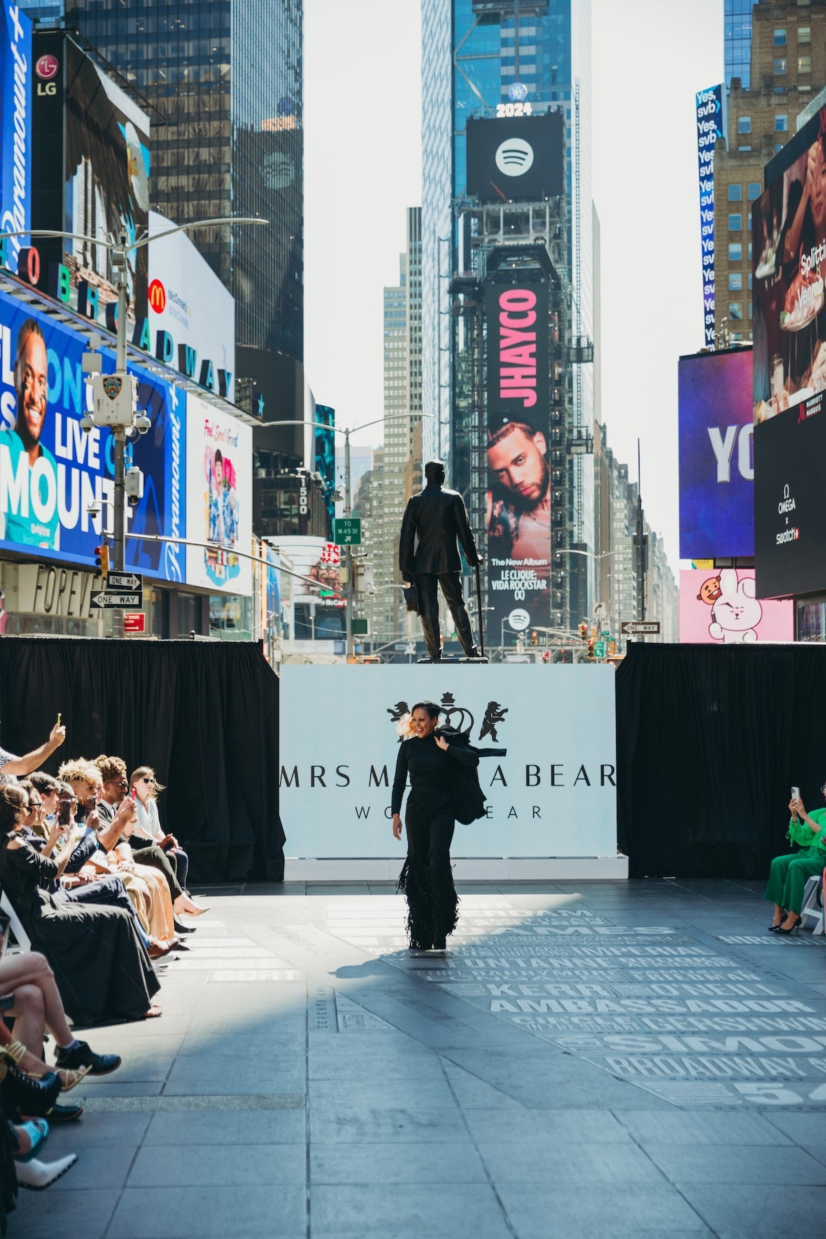 Fashion show in Times Square featuring a model walking on the runway wearing Fringy Baby with vibrant billboards in the background.