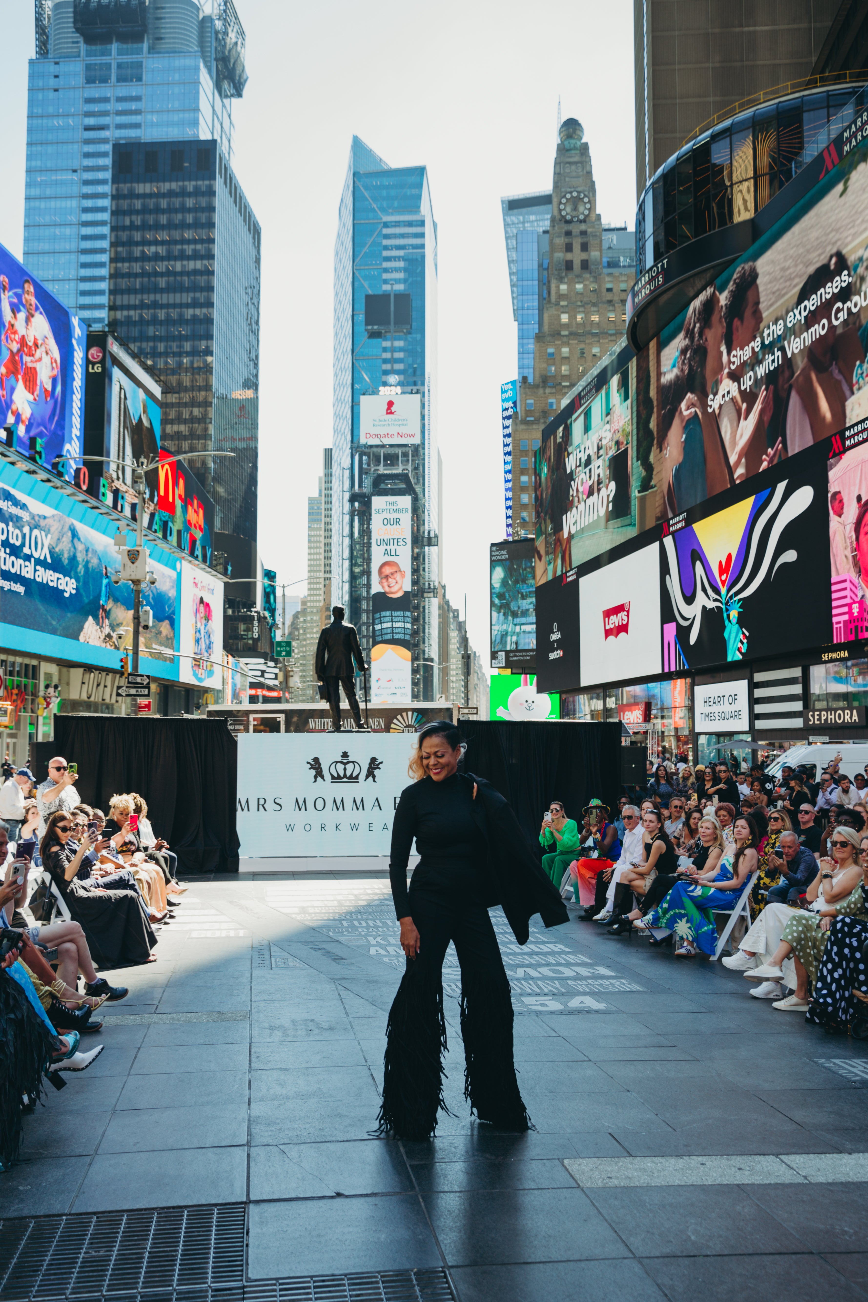 Model showcases Fringy Baby at Times Square fashion event, surrounded by a captivated audience.