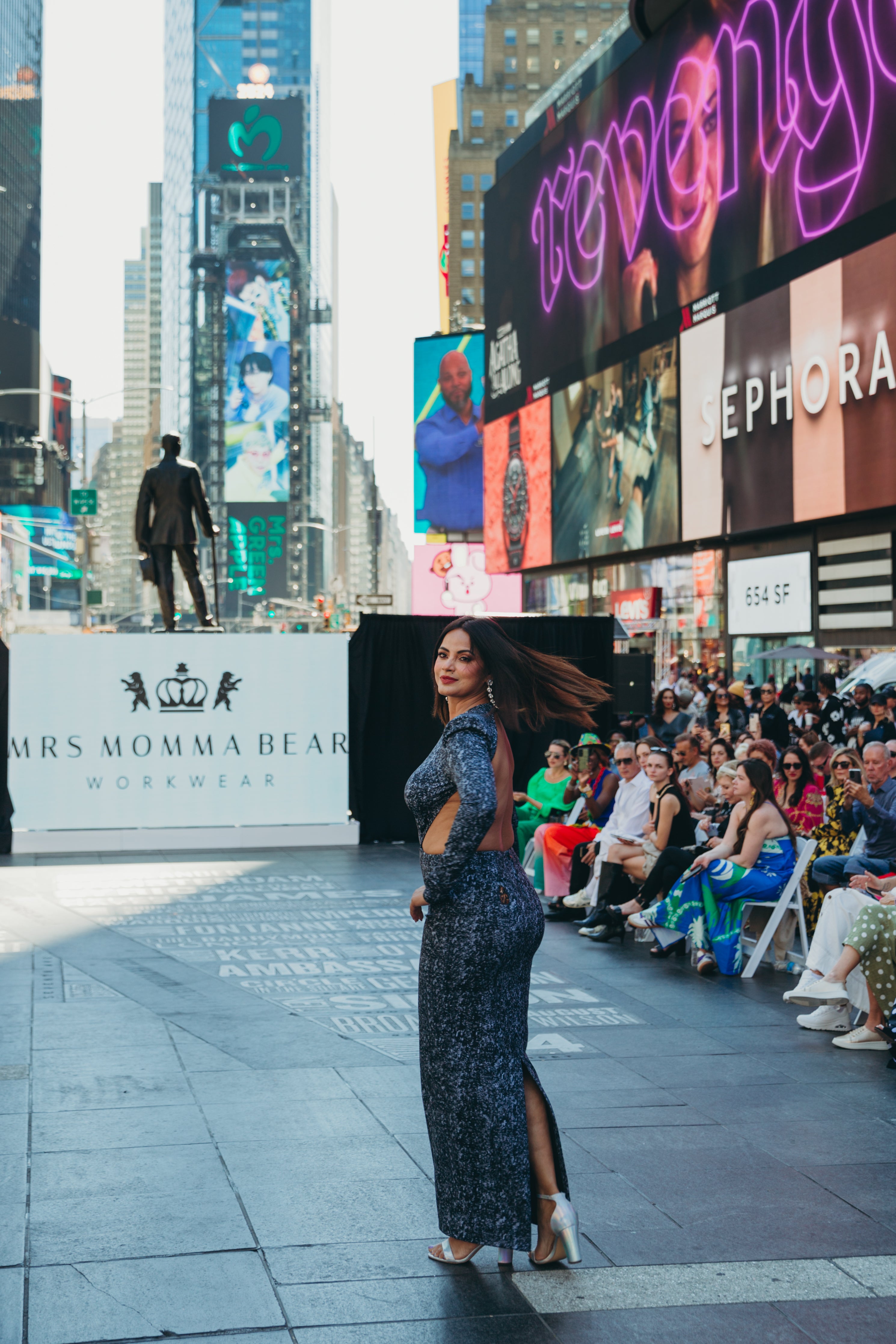 A model showcasing Black Diamond at Times Square during a fashion event with a lively audience and vibrant advertisements in the background.