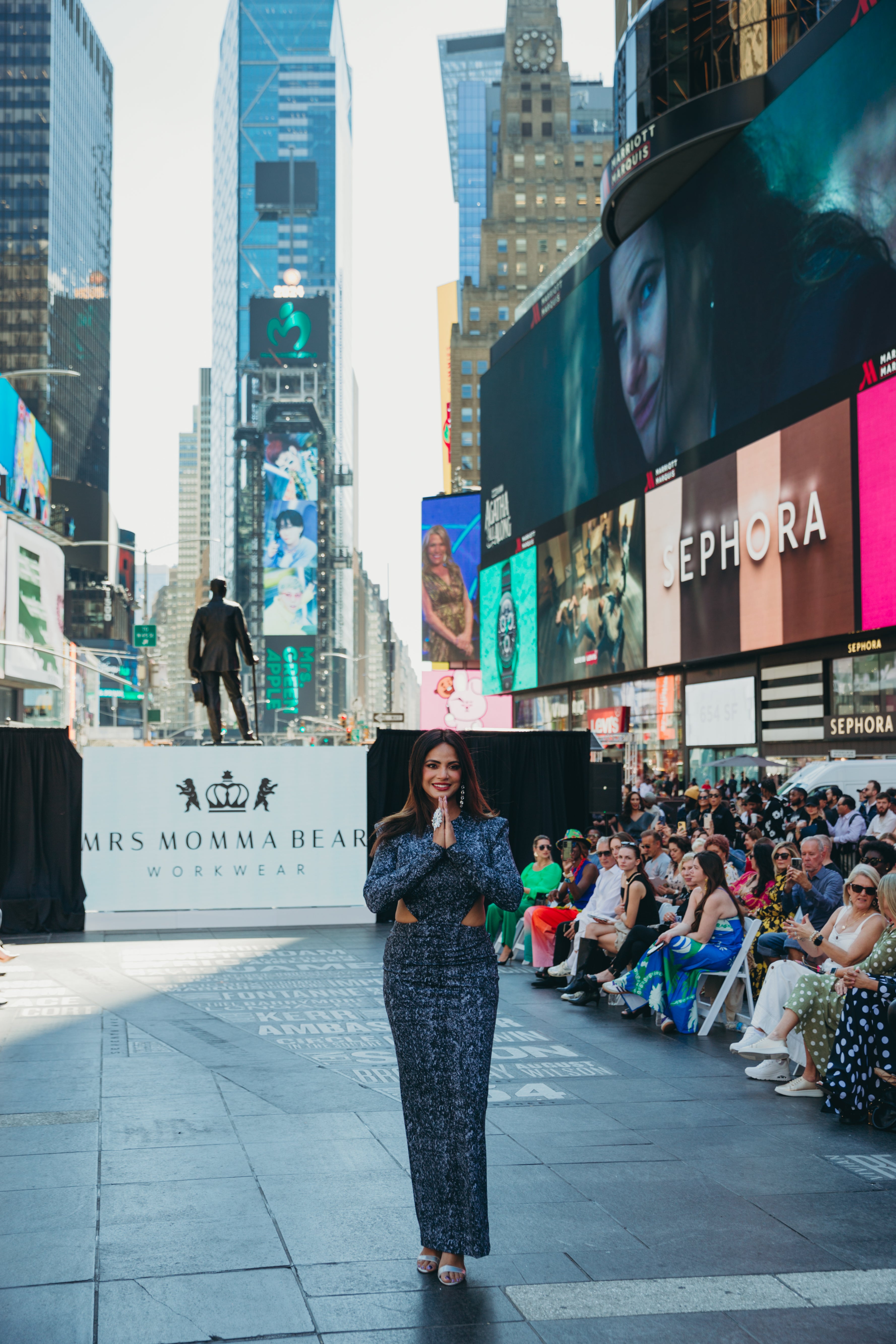 A woman in a Black Diamond speaks at Times Square with large advertisements and a crowd of attendees enjoying the event.