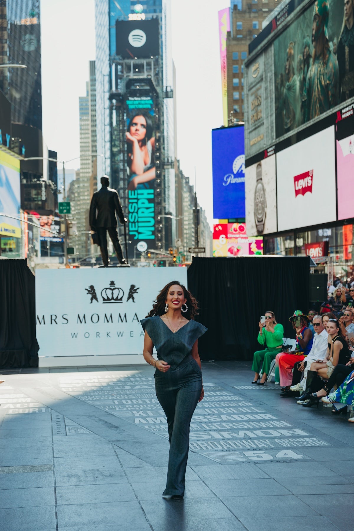 Model wearing Supernova on a runway in Times Square, surrounded by a lively audience and vibrant advertisements.