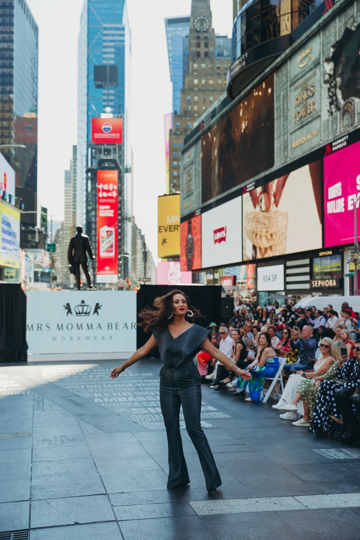 Model wearing Supernova in Times Square for Mrs. Momma Bear fashion event, with vibrant city backdrop and audience present.