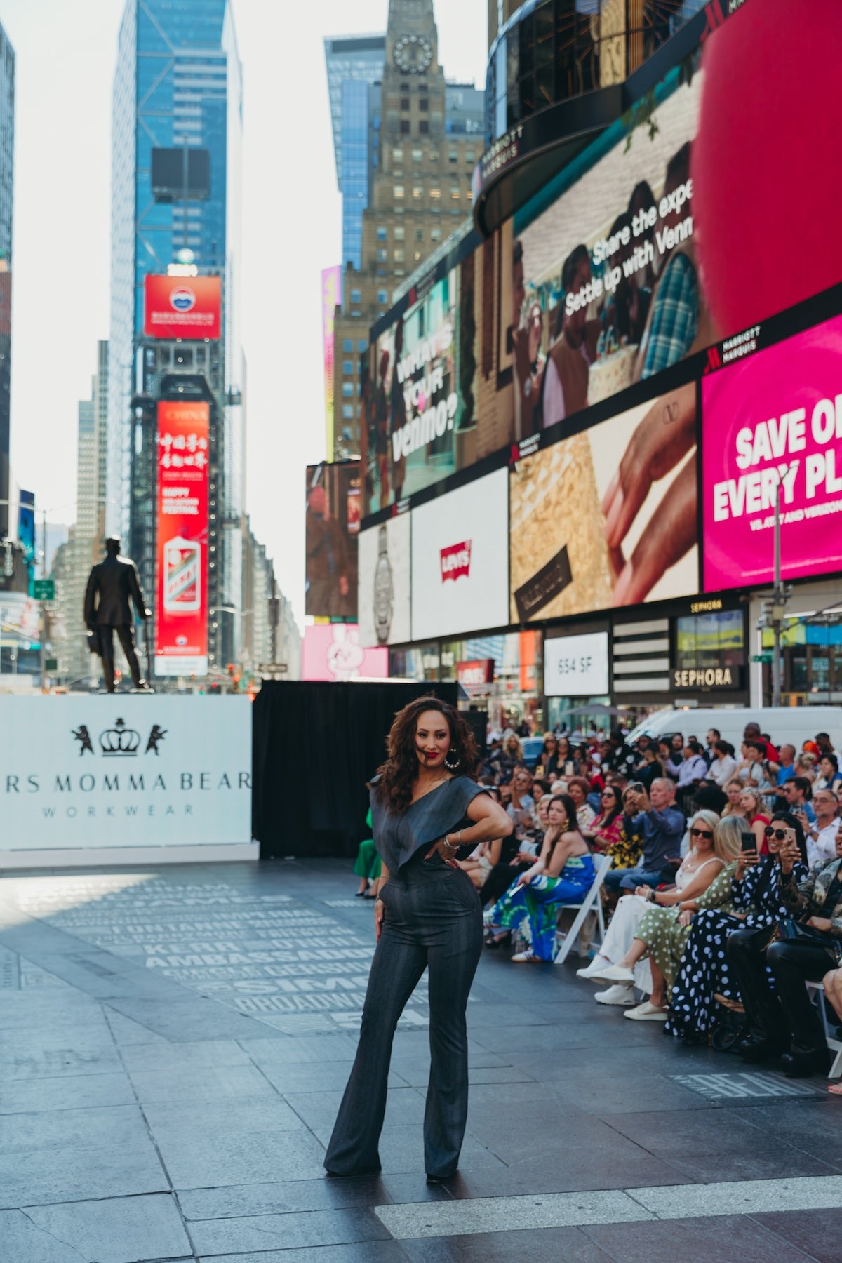 Model poses in Supernova confidently in Times Square fashion show with vibrant billboards and enthusiastic audience in the background.