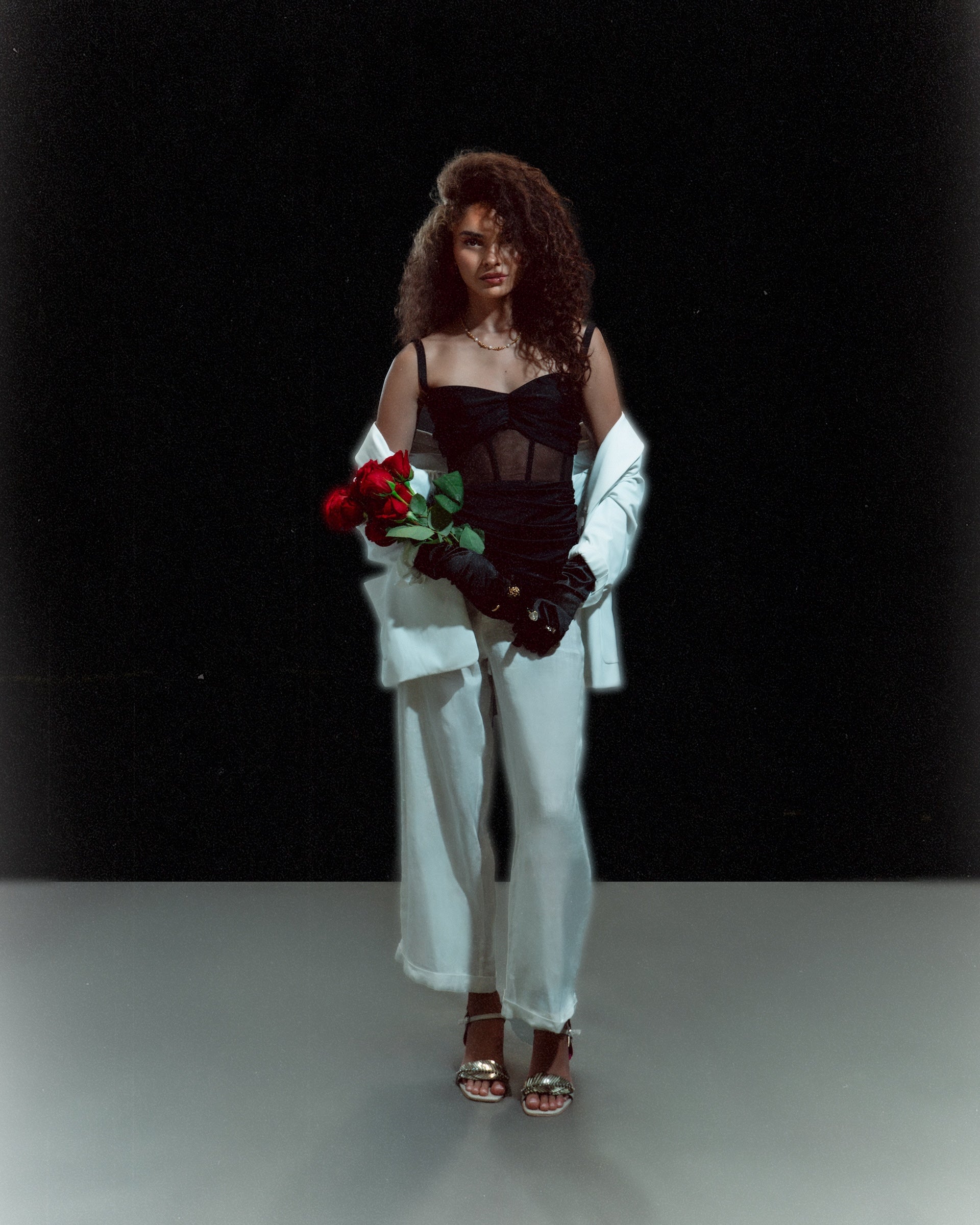 Woman in Meet me at Noon set holding red roses, standing against a dark background with a confident expression.