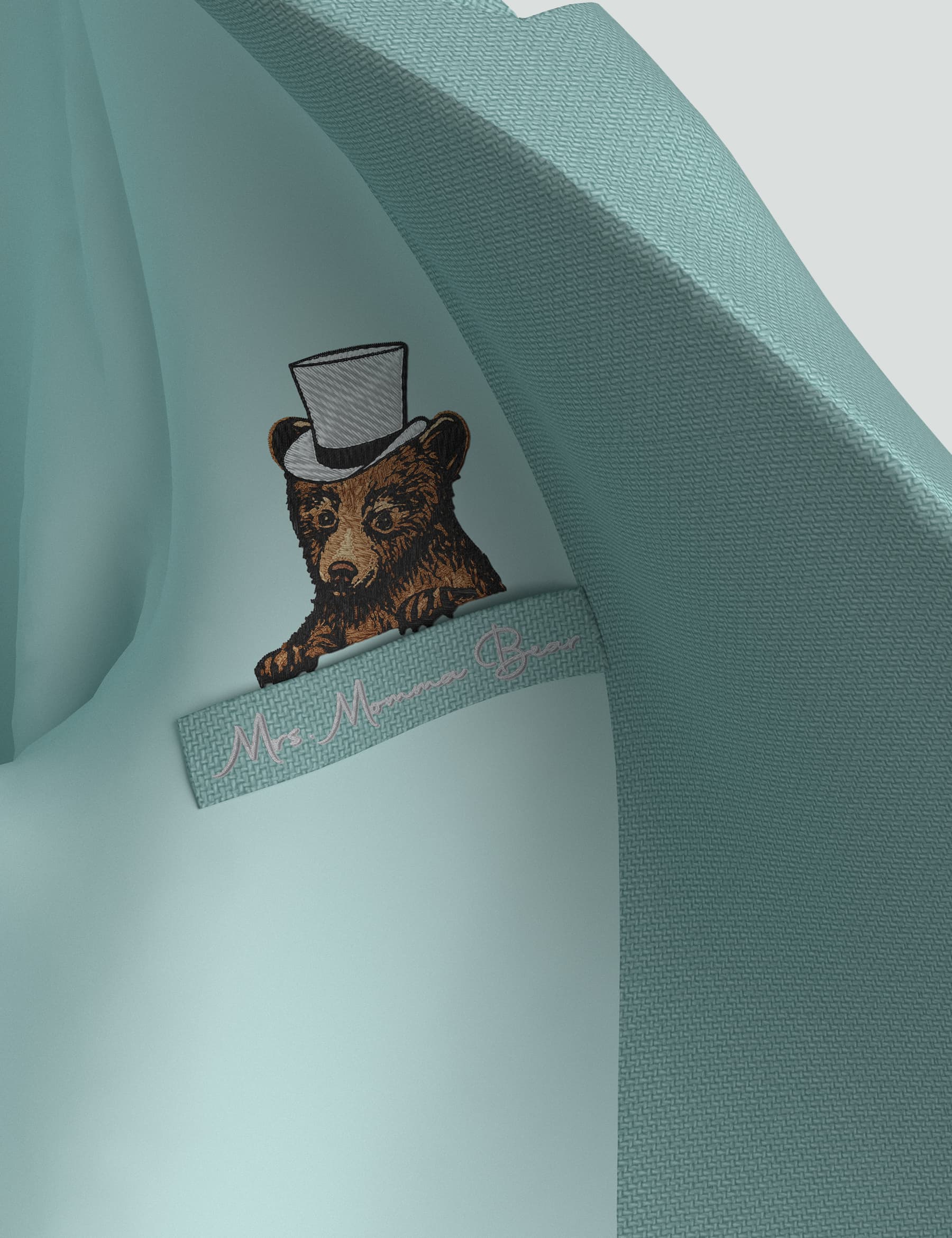 Detail of a mini tuxedo dress featuring a bear logo in a top hat and "Ms. Manners Bear" tag on sea green fabric.