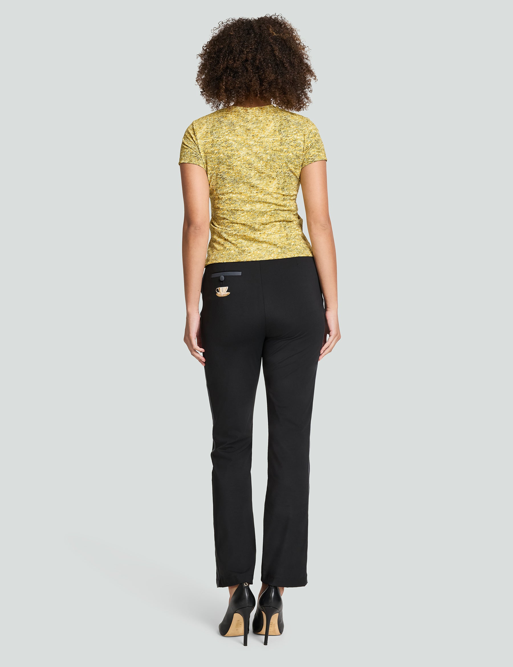 Woman wearing a gold sequin Signature Luxe Tee paired with black pants, showcasing a stylish back view.