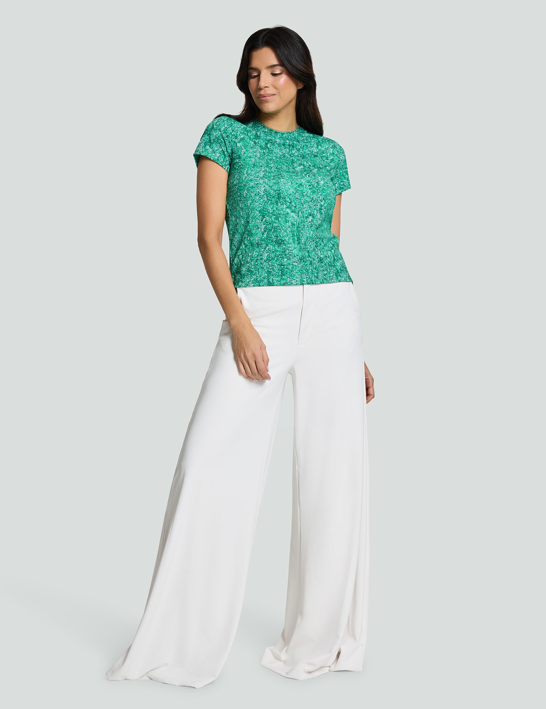 Model wearing Signature Luxe Tee in green sequin print, paired with wide-leg white pants, showcasing a stylish casual look.