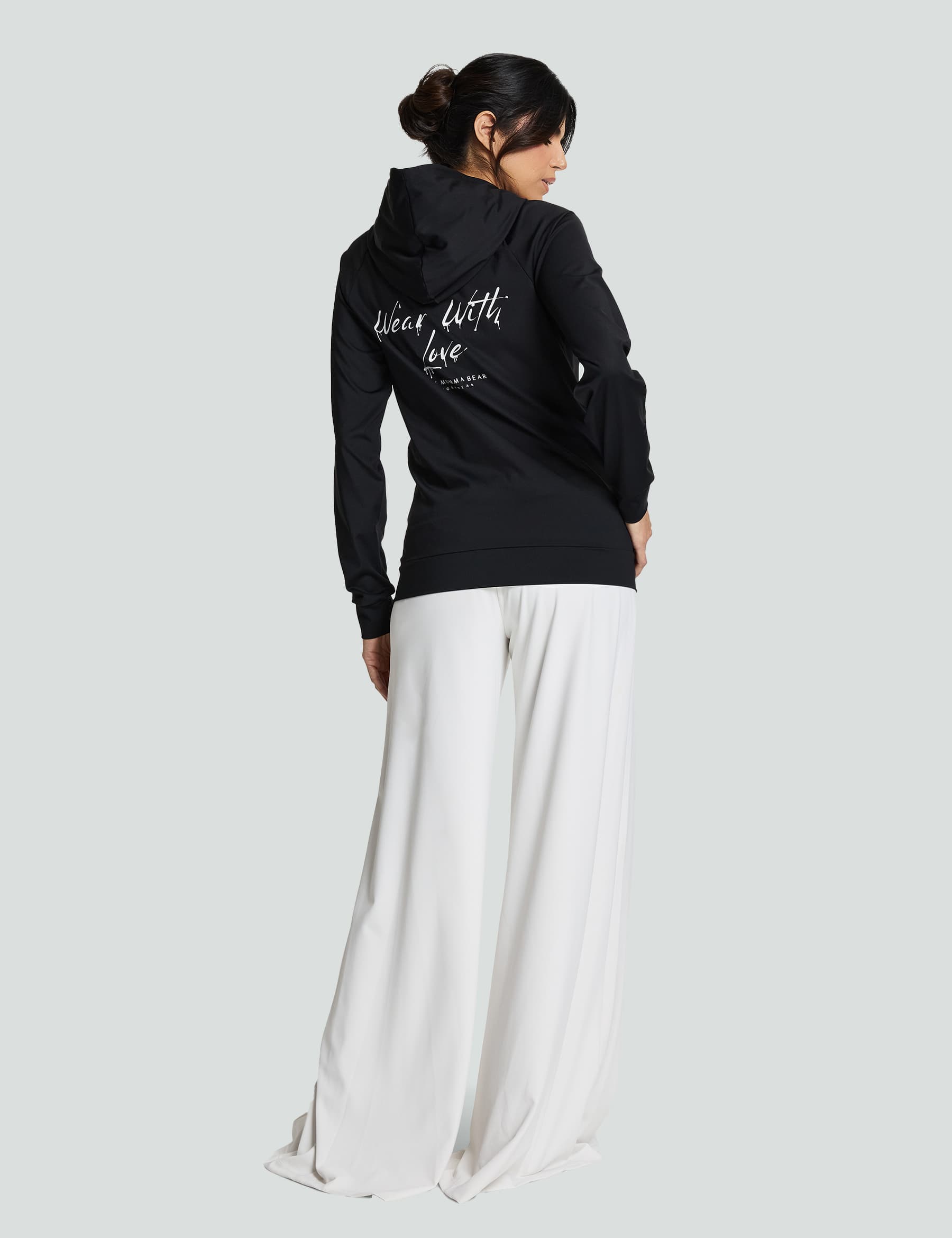 Woman wearing a black hooded sweatshirt with 'Designed with love' text, paired with white wide-leg pants.