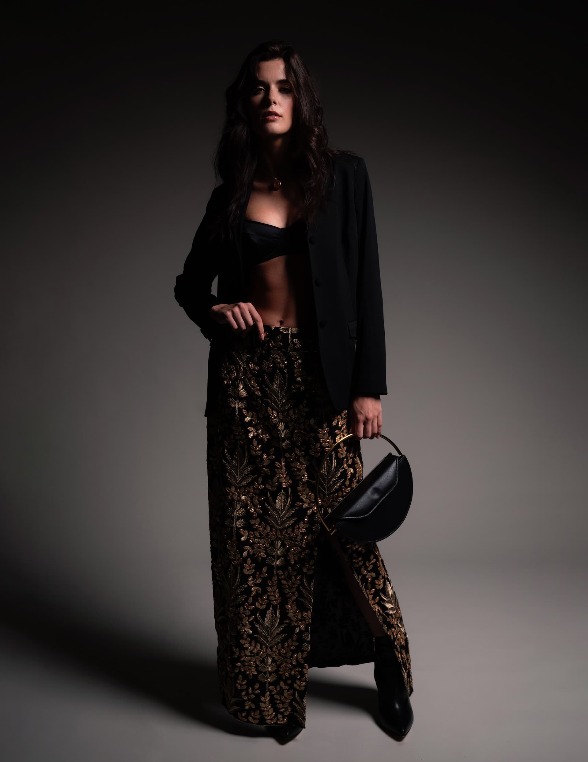 Elegant model in the You Hung the Moon blazer and embellished skirt, posing with a chic handbag against a dark background.