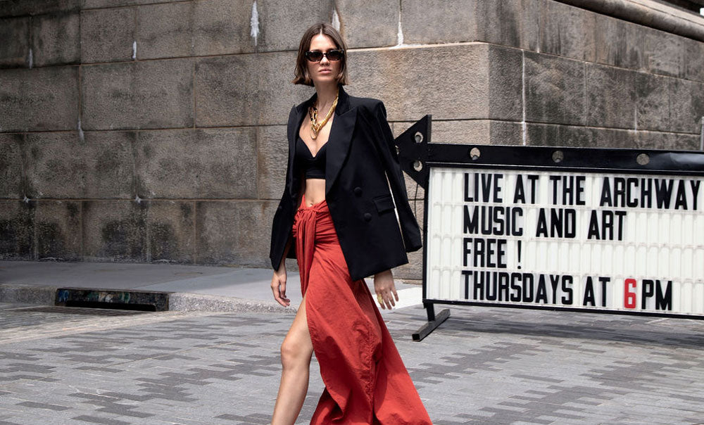 Model wearing the Starry Night blazer over a red gown walking past a sign for a music and art event at the Archway on Thursdays at 6 PM.