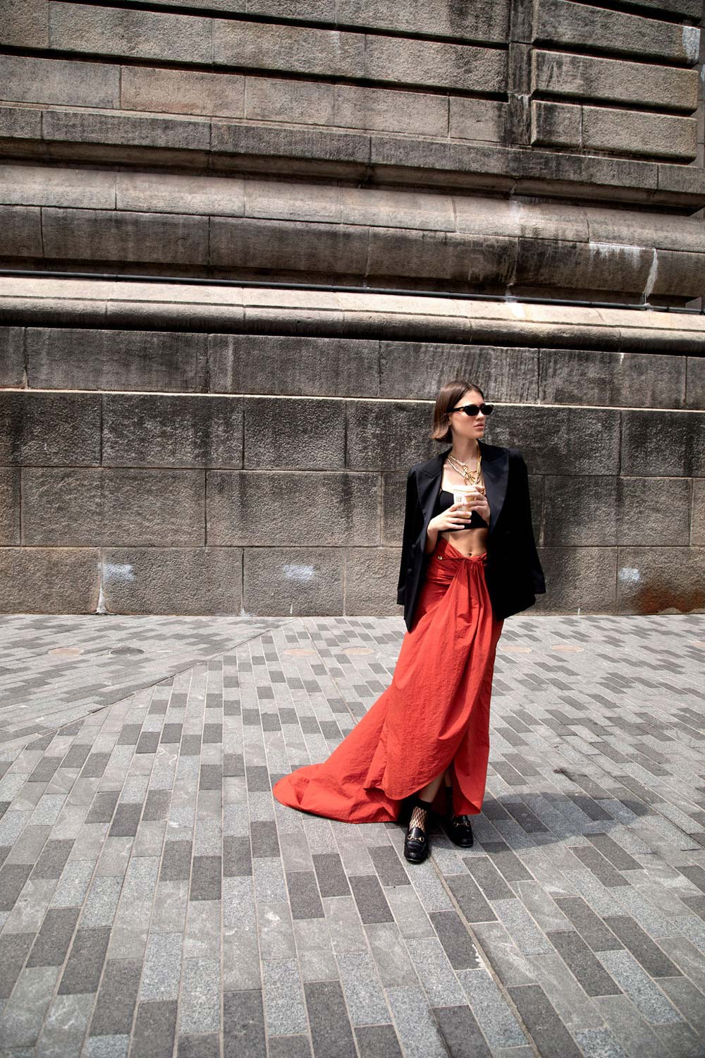 Woman wearing the Starry Night blazer and red skirt stands confidently on patterned pavement against a textured stone wall.